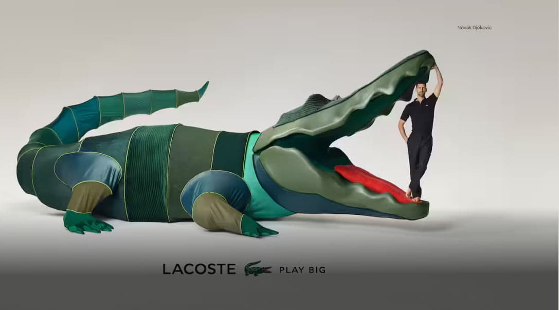 Funny Lacoste ad, a large toy crocodile with a person standing inside its open mouth. The person is wearing casual clothing, and the Lacoste logo and slogan 'Play Big' are displayed beneath the image.